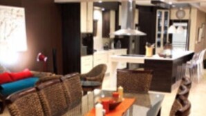 Un salon moderne avec une table à manger au plateau en verre, entourée de chaises en osier dotées de coussins bleus.