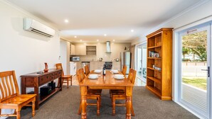 Een eetgedeelte met een houten tafel, gedekt voor zes personen, met aan weerszijden stoelen, een houten boekenkast en een keuken op de achtergrond.