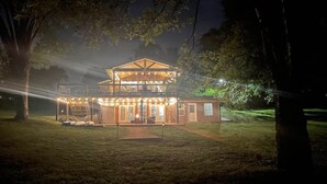 A two-story building with a porch and string lights, surrounded by trees. - Lakefront | Sauna | Kayaks | Firepit | 35 Min to Nashville (Gallatin)