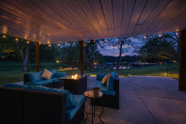Une terrasse extérieure aménagée avec des meubles en osier, un foyer et des guirlandes lumineuses.