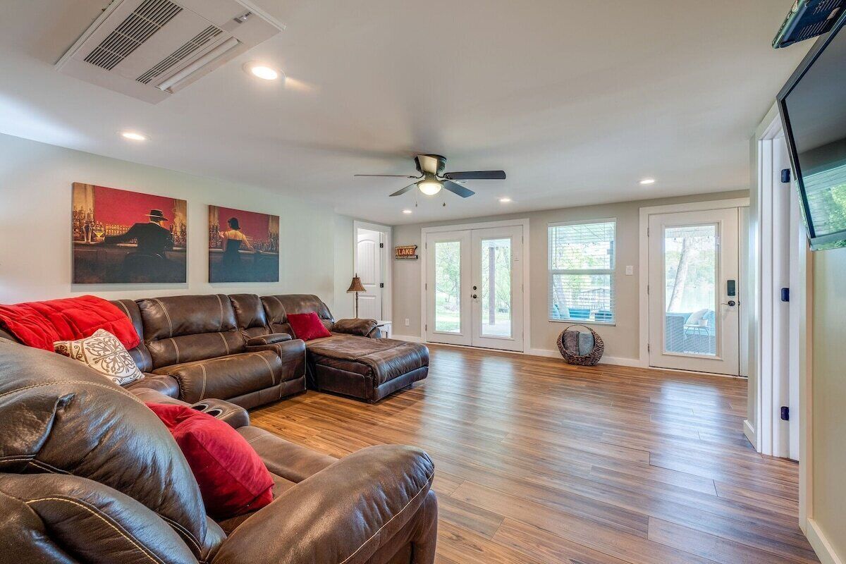 A spacious living room with a large leather sectional sofa, hardwood flooring, and a ceiling fan.