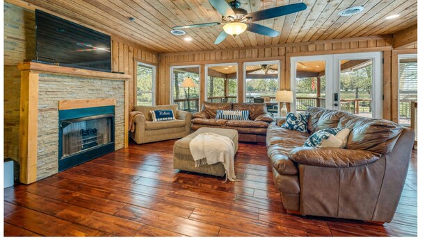 A spacious living room with a fireplace, leather sofas, and a ceiling fan. - Lakefront | Sauna | Kayaks | Firepit | 35 Min to Nashville (Gallatin)