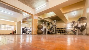 Un gimnasio amplio con equipo de ejercicio, ventanas grandes y suelo pulido.