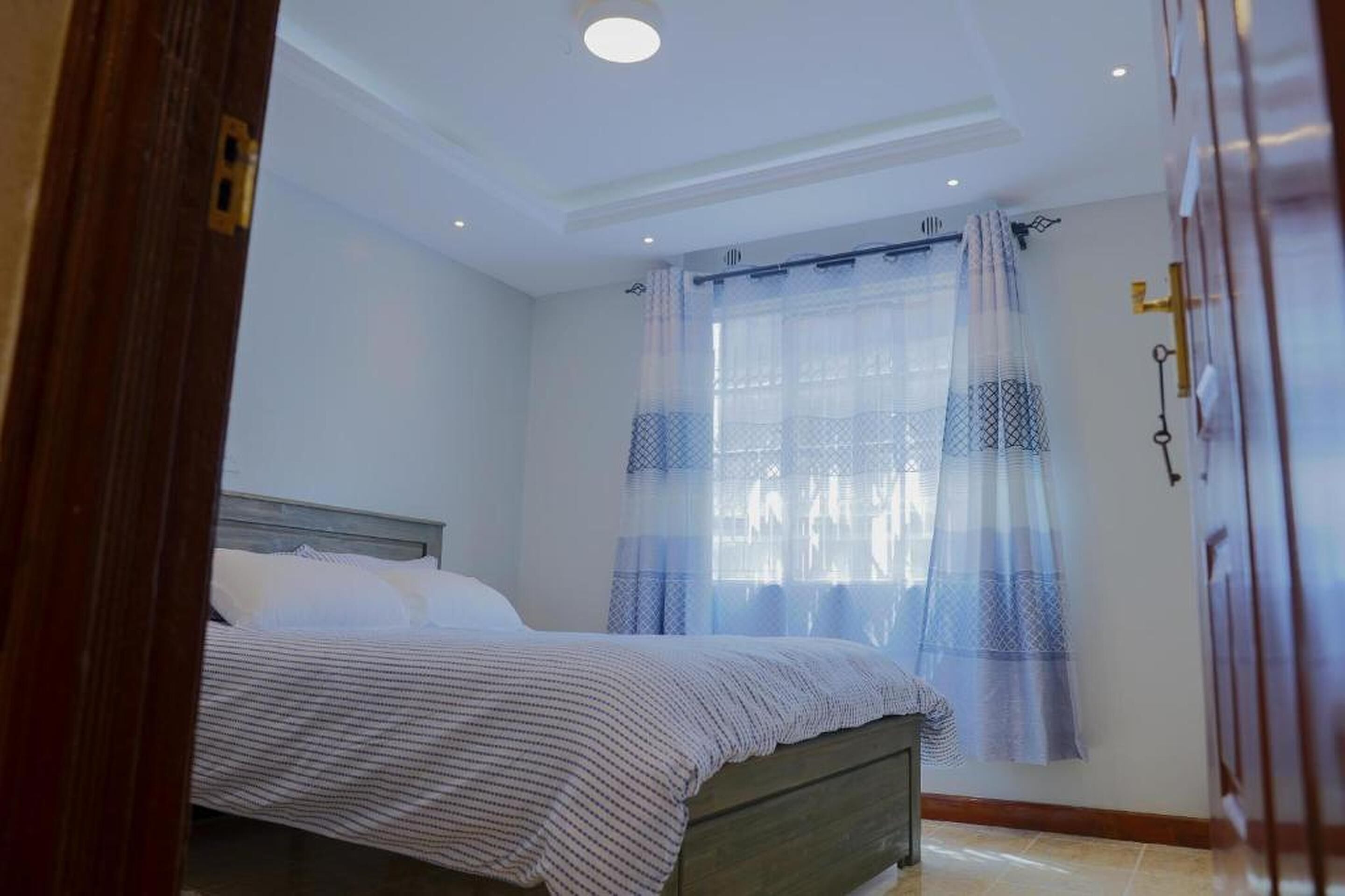 Un dormitorio con una cama, una ventana con cortinas translúcidas y una puerta de madera.