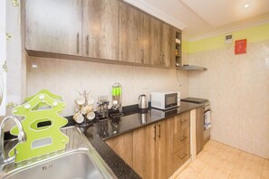 Cocina con armarios de madera, encimera negra, microondas y hervidor.