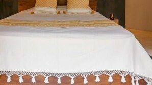 Cama com colcha branca e um adorno pendurado acima.