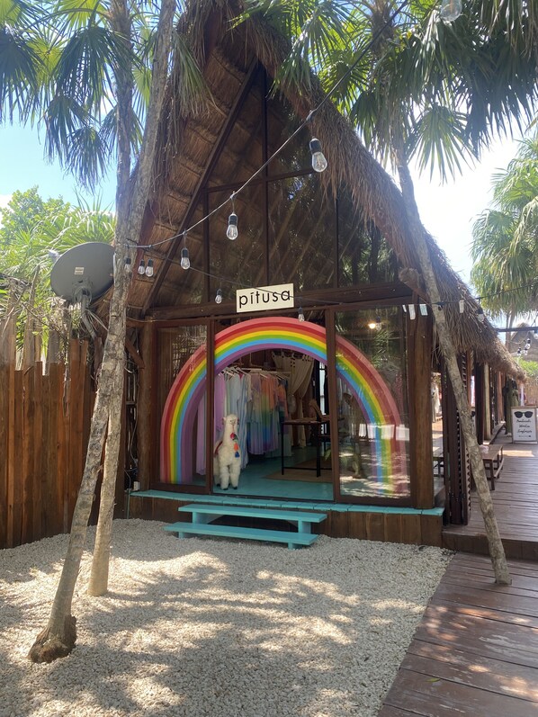 Un bâtiment rustique avec un toit de chaume, une enseigne indiquant « pitusa », et une arche en forme d’arc-en-ciel.