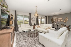 A modern living room with a sectional sofa, a glass coffee table, and a chandelier. - Movie Nights in Private Theater! EPIC Outdoor Living! Resort Near Disney! (Kissimmee)