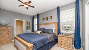 Une chambre à coucher avec un lit, des tables de chevet en bois, un ventilateur de plafond et une fenêtre avec des rideaux.
