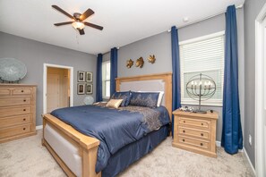 A bedroom with a bed, wooden nightstands, a ceiling fan, and a window with curtains.