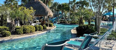 A pool area with lounge chairs, a thatched structure, palm trees, and a clear blue sky.