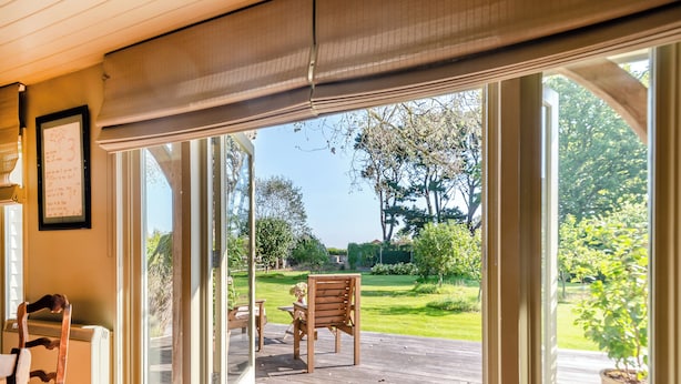 Una habitación con puerta corrediza de vidrio que da a un patio exterior con terraza de madera, una silla y una mesita.