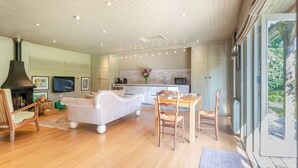 Una sala de estar moderna con chimenea, un sofá, una mesa de comedor con sillas, una zona de cocina y ventanas amplias.