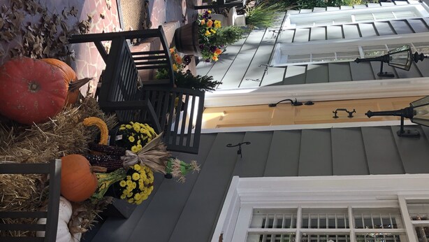 A view of a house's exterior with a dark gray roof, a white window with a grid pattern, and a wooden fence with pumpkins and flowers. - Exclusive Myers Park RNC Rental 4000 sq ft Home - RENOVATED 15 min. to downtown (Charlotte)