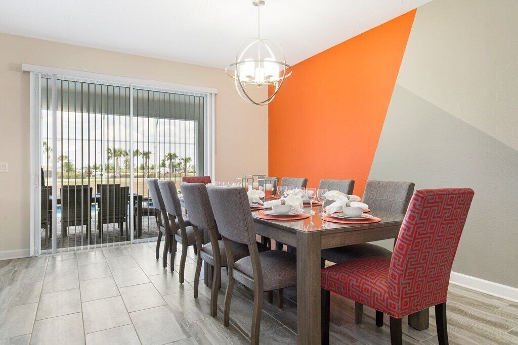 A dining area with a table set for four, chairs, and a view through a sliding door to an outdoor area with palm trees.
