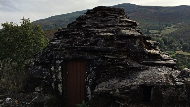 Une cabane en pierre avec une porte en bois, entourée d’un paysage naturel et de montagnes.