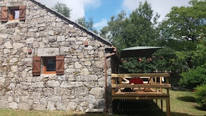 Un bâtiment en pierre avec des volets en bois et une terrasse en bois comprenant une table et des chaises.