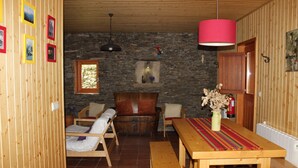 Une pièce chaleureuse avec un plancher en bois, un mur en pierre, un banc en bois, une table recouverte d’une nappe rouge et une lampe rouge suspendue au plafond.