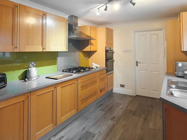 A modern kitchen with wooden cabinets, a gas stove, an oven, and a white door.