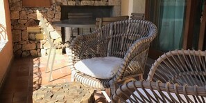 Cadires de vimet amb coixins, una paret de pedra i un terra de rajola.
