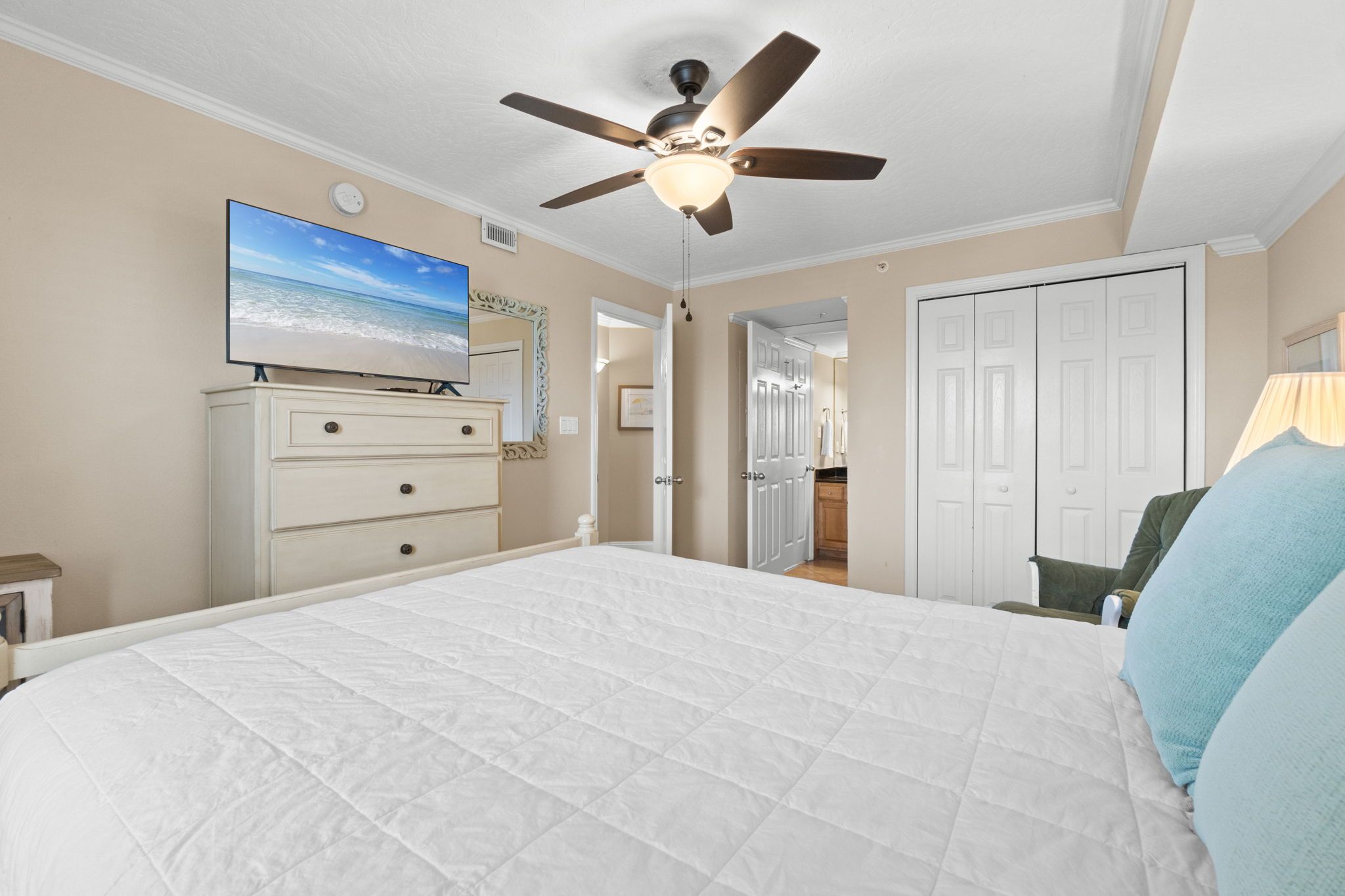 Een slaapkamer met een bed, plafondventilator, televisie, dressoir en een deur.