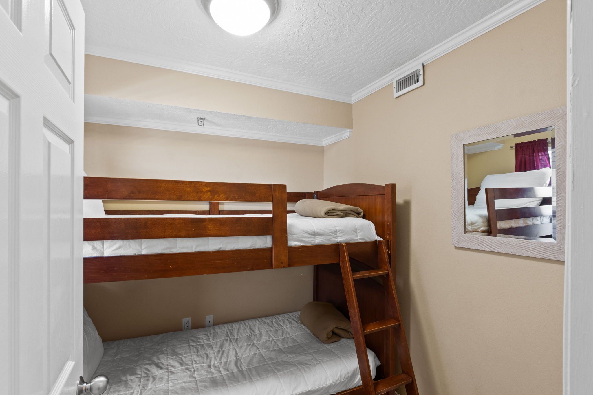 A bunk bed room with a ladder, a mirror, and a ceiling light fixture.