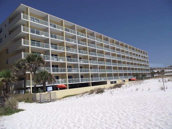 Un hôtel à plusieurs étages, doté de balcons, situé près d’une plage de sable.