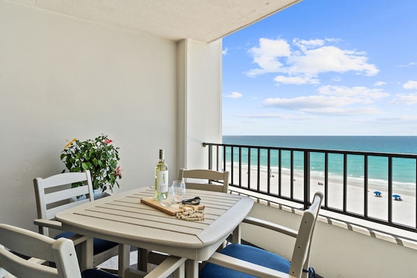 A balcony with a table set for two, a potted plant, and a view of the beach. - Surf Dweller 703 - Solstice Shores (Fort Walton Beach)