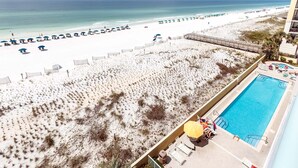 A beach resort with a swimming pool, beach umbrellas, and a view of the ocean. - Pelican Isle 507 - Breezy Bliss (Fort Walton Beach)