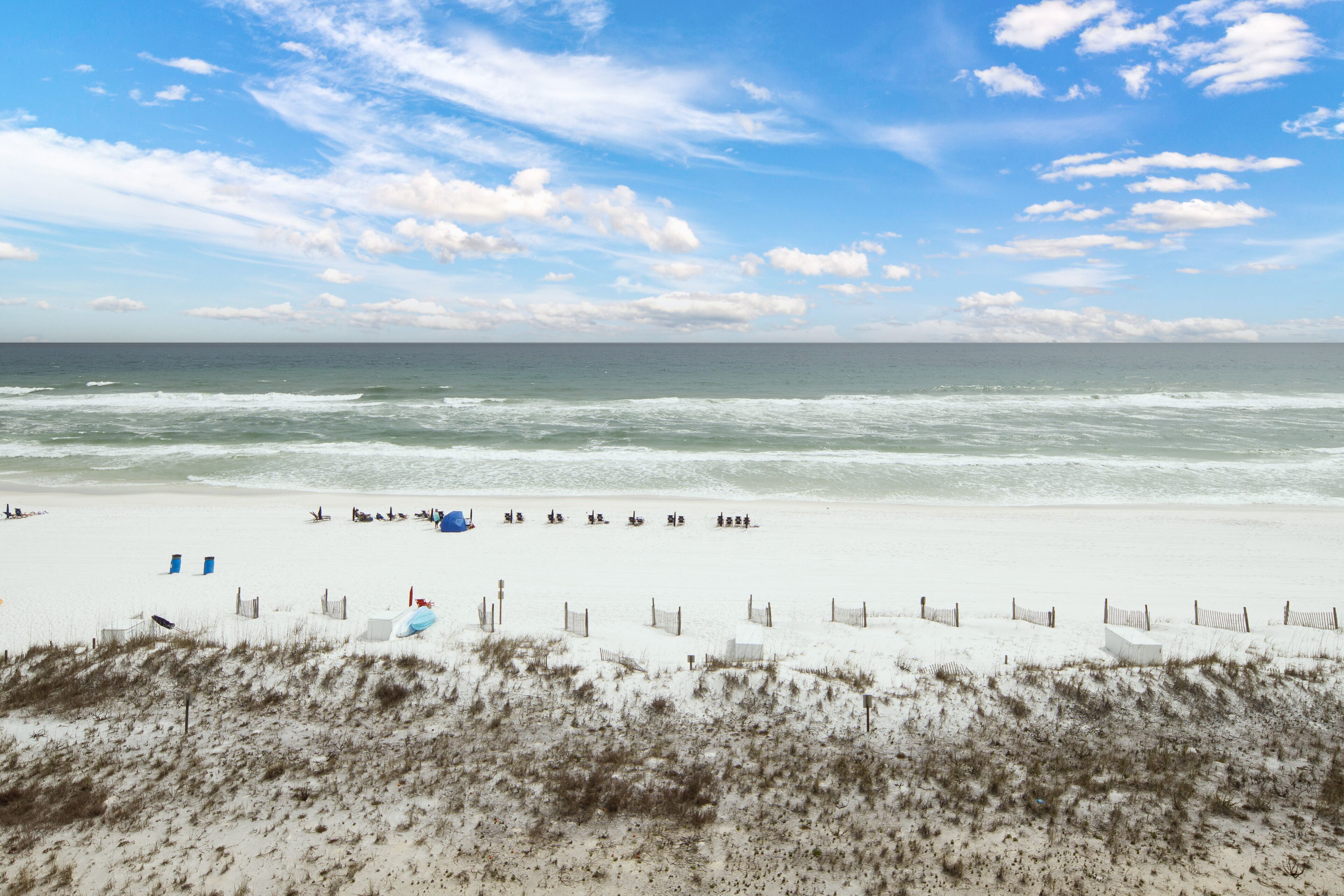 Une plage avec un rivage sablonneux, quelques personnes et un ciel dégagé.