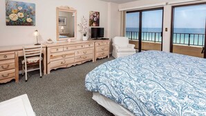 A hotel room with a bed, a desk, a chair, a TV, a dresser, and a balcony with a view of the sea. - Surf Dweller 709 - Tidal Treasures (Fort Walton Beach)