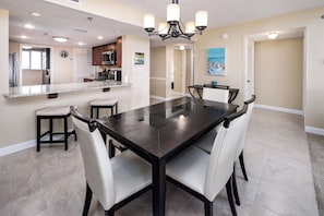 A modern kitchen with dark countertops, white chairs, and a central island. - Surf Dweller 510 - Coastal Canvas (Fort Walton Beach)