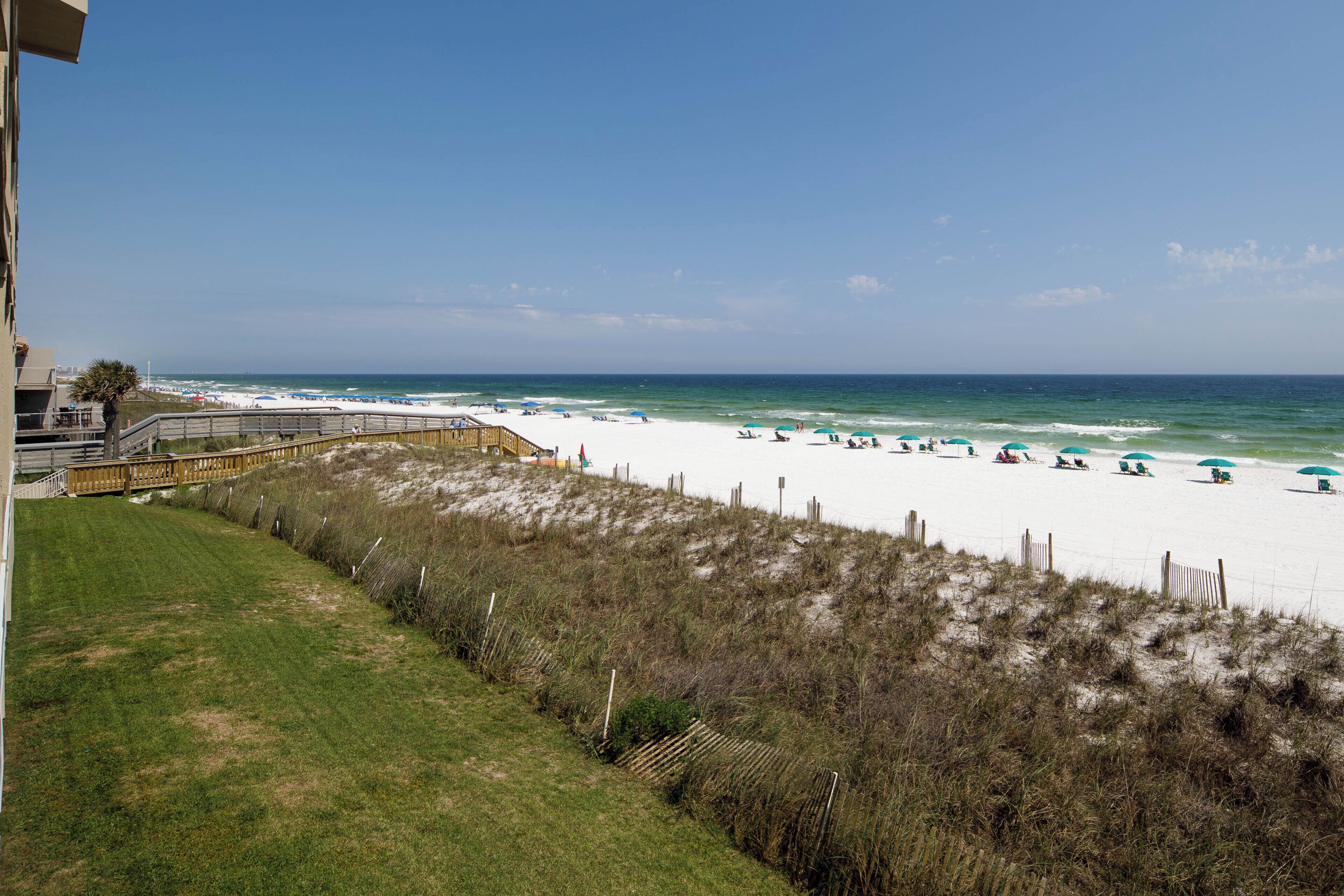 A beach with white sand, a wooden boardwalk, and beach umbrellas.