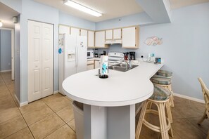 A modern kitchen with white cabinets, a central island, bar stools, and a microwave. - Emerald Towers West 2005 - Emerald Shore (Fort Walton Beach)