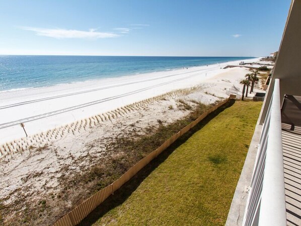 A beach view from a balcony with a clear sky, a sandy beach, and a grassy area. - Emerald Twrs West 3003 by Brooks and Shorey Resorts (Fort Walton Beach)