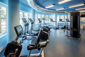 Een fitnessruimte met cardioapparatuur, krachttrainingsapparatuur en grote ramen.