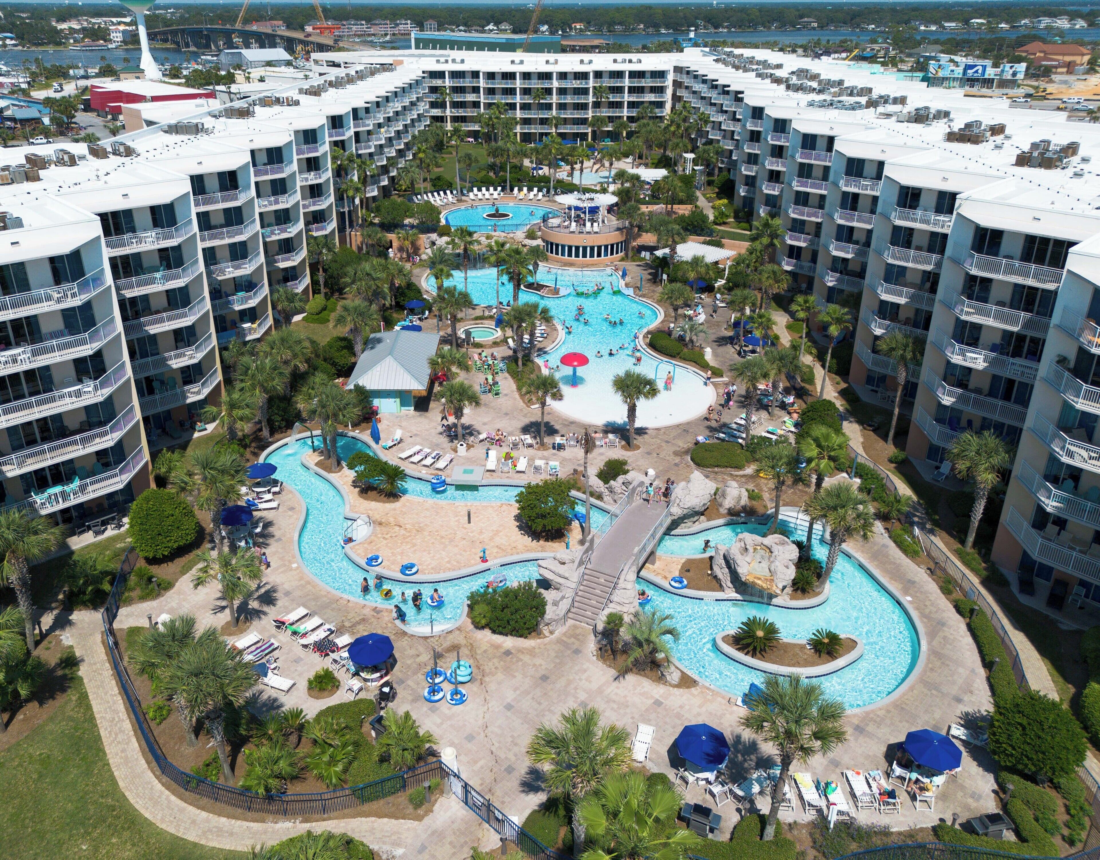 A large resort with multiple swimming pools, palm trees, and a central water slide.
