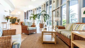 A spacious lobby with wicker furniture, large windows, and potted plants. - Waterscape B310 - Resort Shores (Fort Walton Beach)
