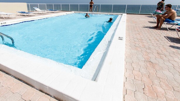 A rectangular swimming pool with clear blue water, surrounded by a tiled deck and a metal railing. - Gulfside 302 - Ocean Serenity (Fort Walton Beach)