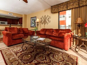 A living room with a red velvet sofa, a glass coffee table, and a patterned rug. - Gulfside 501 - Sandy Adventures (Fort Walton Beach)