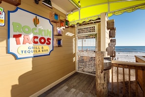 Un restaurant situé en bord de mer, appelé « Rockin Tacos », avec une enseigne, une terrasse en bois et une vue sur la plage.