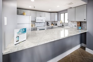A modern kitchen with grey cabinets, a white countertop, and a built-in microwave. - Gulfside 501 - Sandy Adventures (Fort Walton Beach)