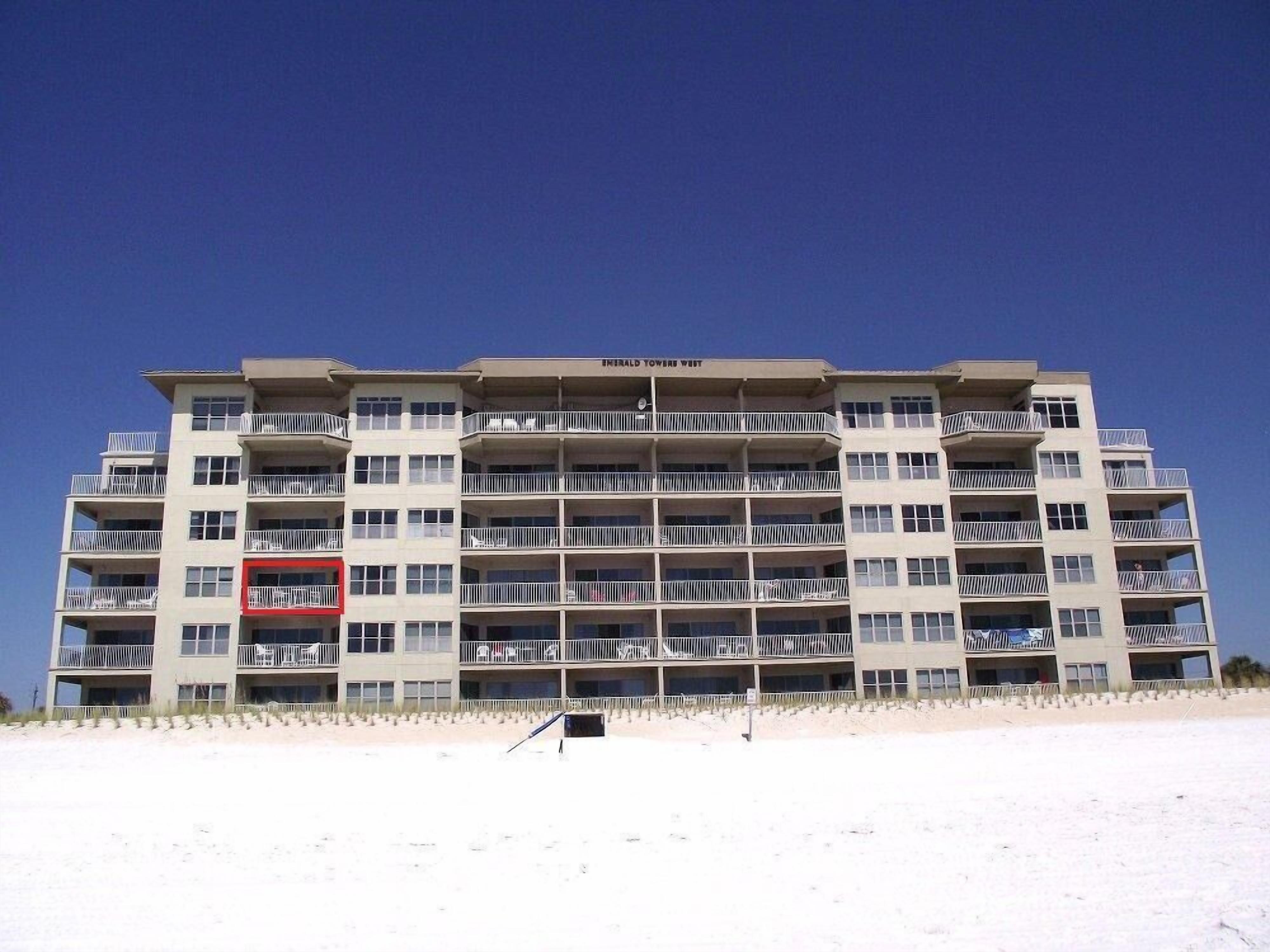 A multi-story hotel with balconies, located near a beach.