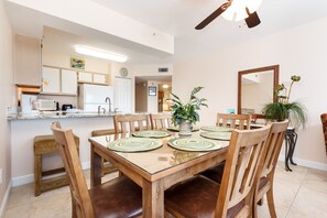 Zona pranzo con tavolo in legno, sedie e cucina sullo sfondo.