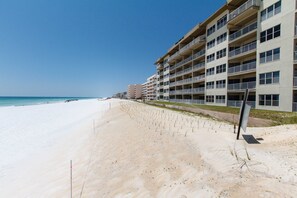 A beachfront hotel with multiple balconies, a sandy beach, and a clear blue sky. - Emerald Towers West 1003 - Sandy Toes (Fort Walton Beach)