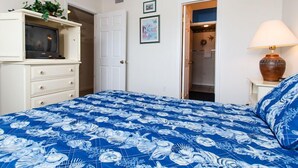 A bedroom with a bed, a television on a cabinet, a door, and a lamp. - Emerald Towers West 1003 - Sandy Toes (Fort Walton Beach)