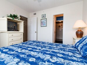 A bedroom with a bed, a television on a cabinet, a door, and a lamp. - Emerald Towers West 1003 - Sandy Toes (Fort Walton Beach)