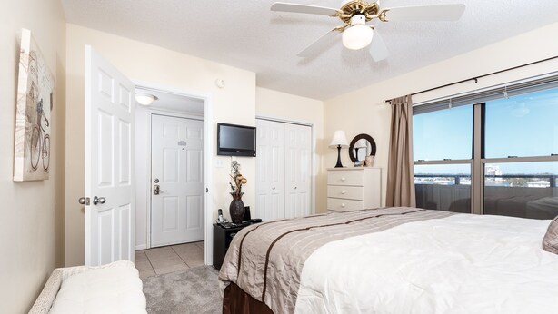 A bedroom with a large bed, a ceiling fan, a TV, a dresser, and a window with a view. - Emerald Towers West 5004 - Beachside Memories (Fort Walton Beach)