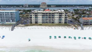 A beachfront hotel with multiple floors, a pool, and beach umbrellas. - Emerald Towers West 5004 - Beachside Memories (Fort Walton Beach)