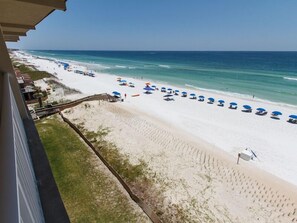 A beach with white sand, blue umbrellas, and a wooden walkway leading to the shore. - Emerald Towers West 5004 - Beachside Memories (Fort Walton Beach)